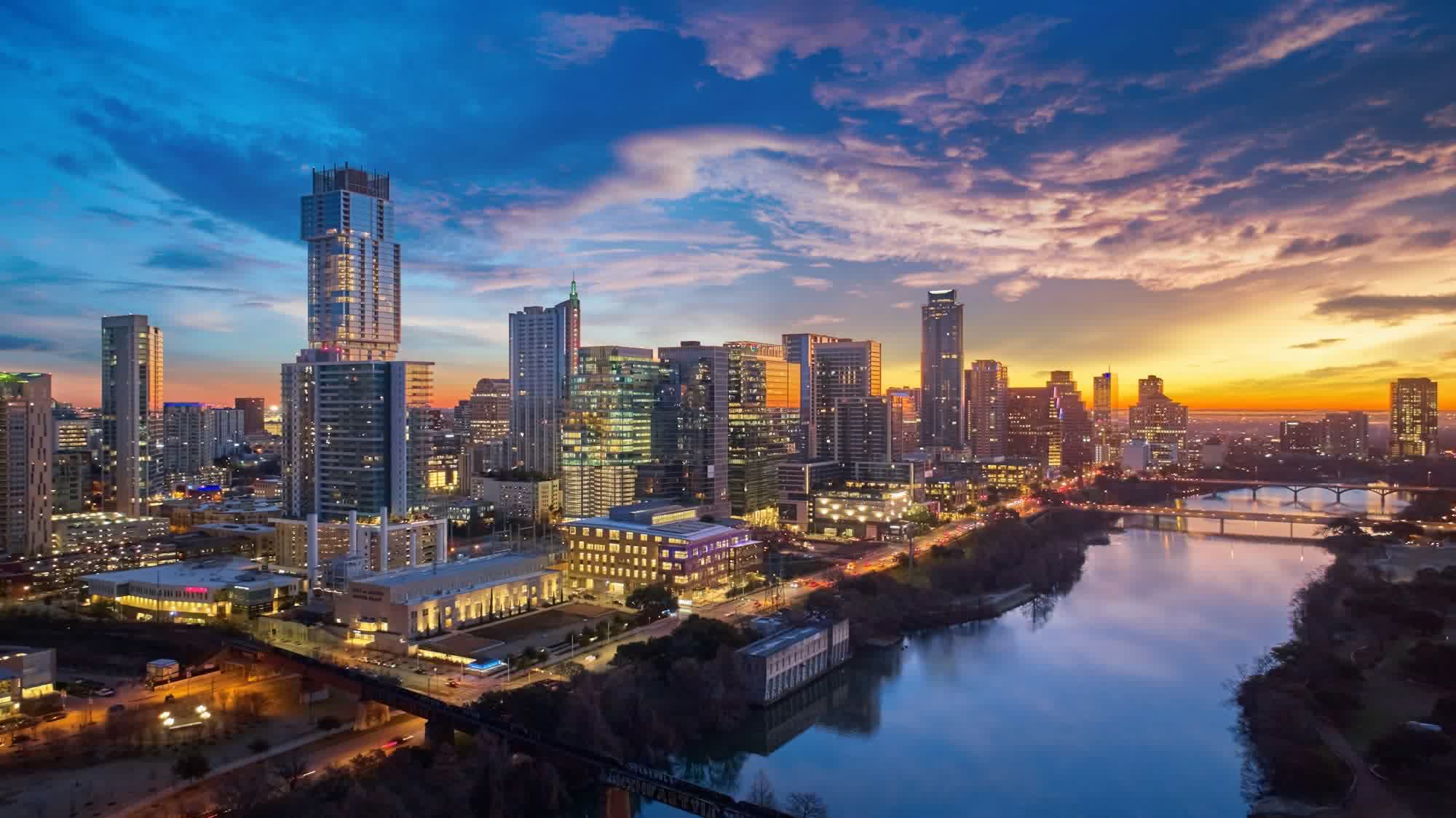 A downtown skyline over a river at dusk with traffic crossing the bridges