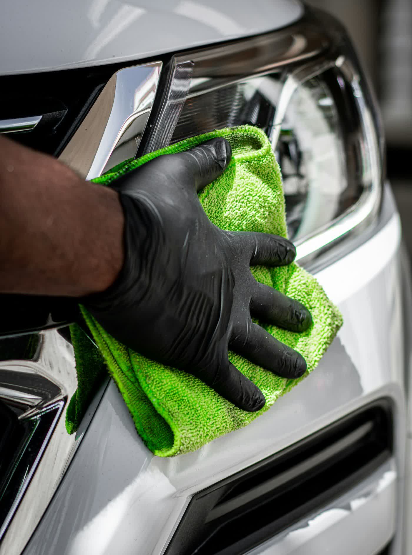 A gloved hand drawing a microfiber towel across a front end beside the headlight