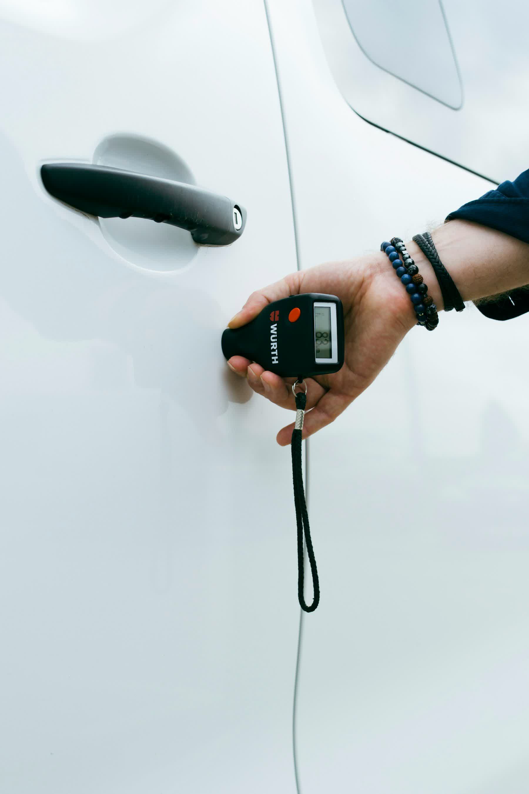 A paint depth gauge held against the white door of a car
