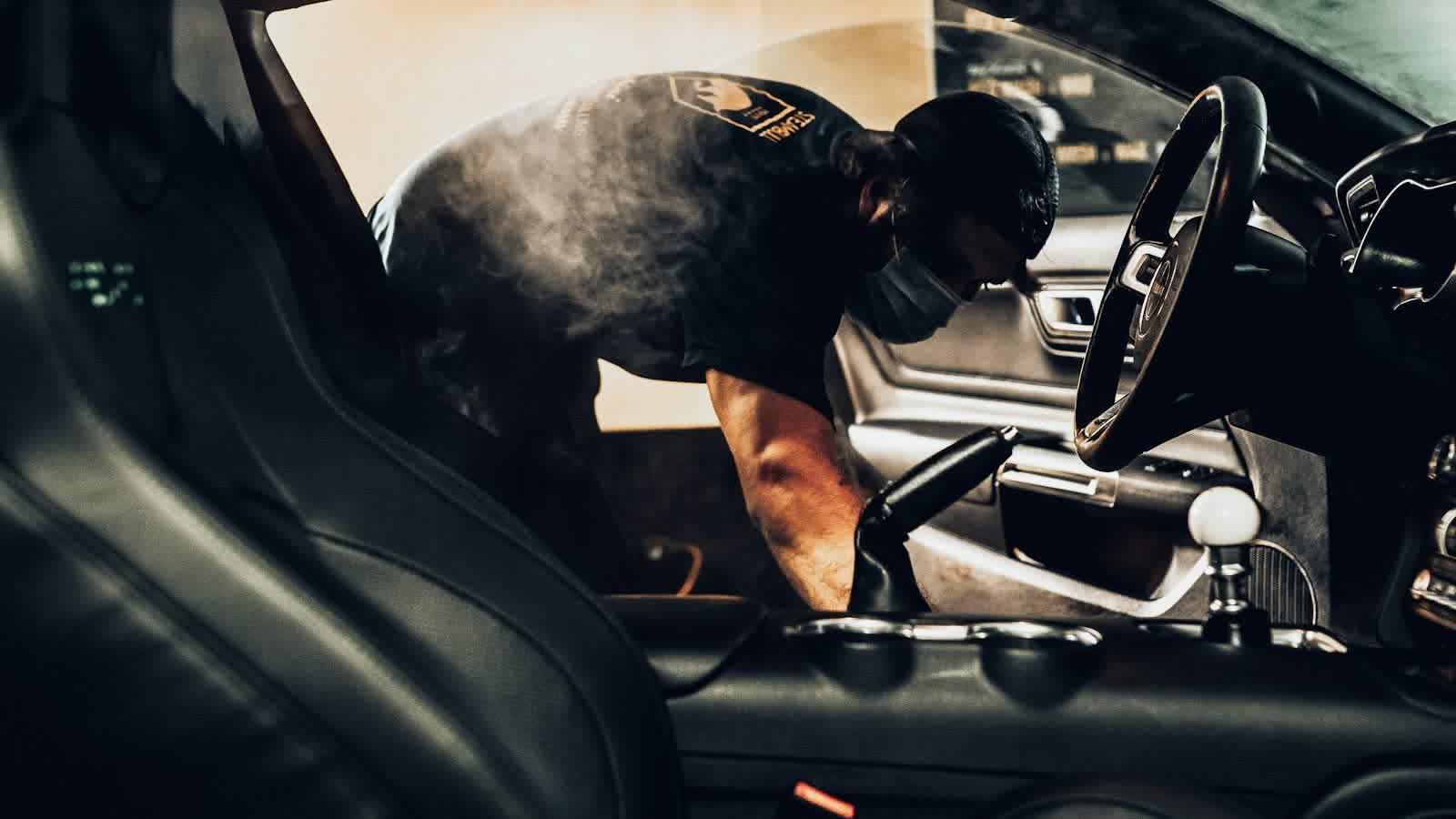 A technician steam cleaning the driver's side of a car cabin