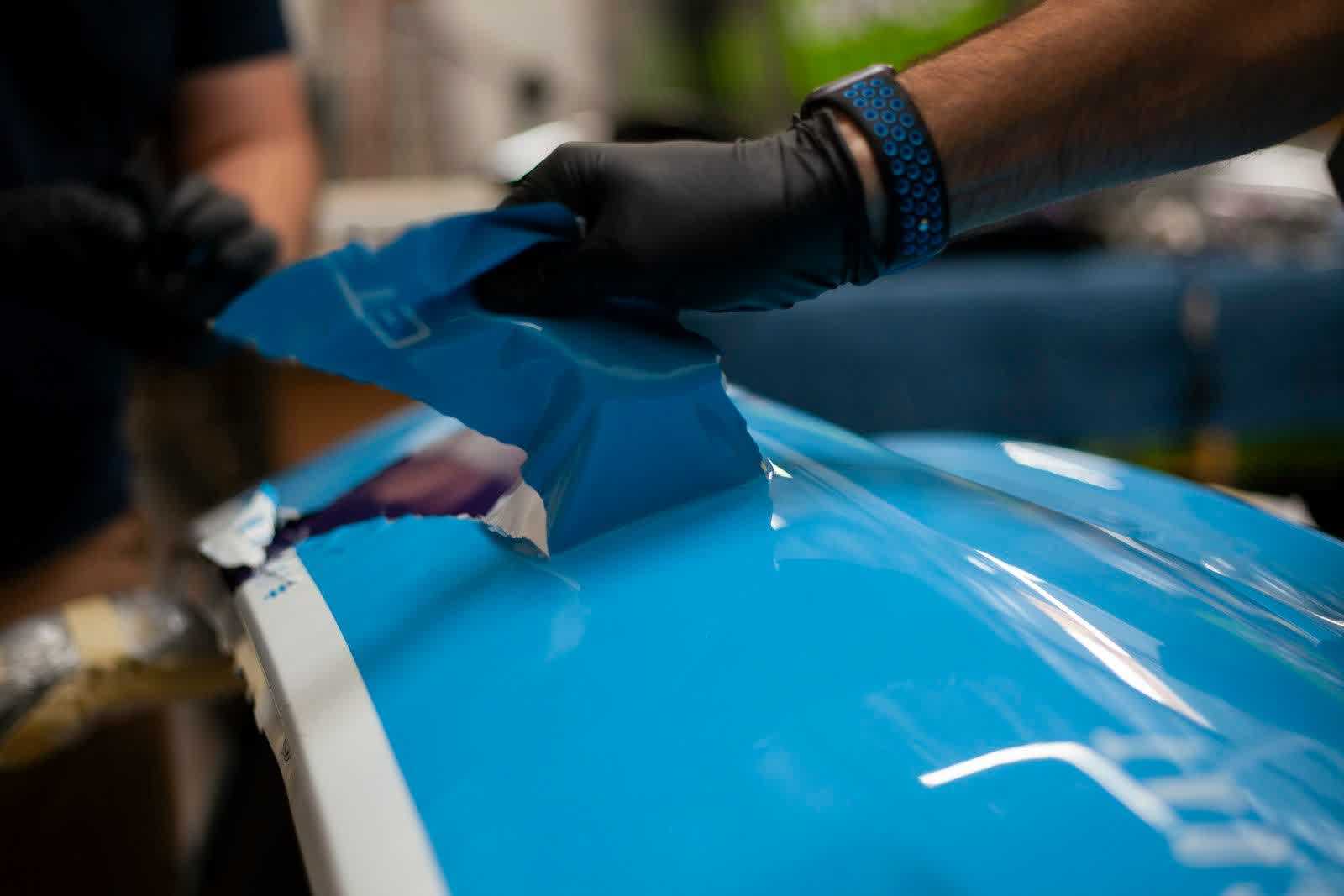 Gloved hands lifting a cut sheet of protection film over a hood