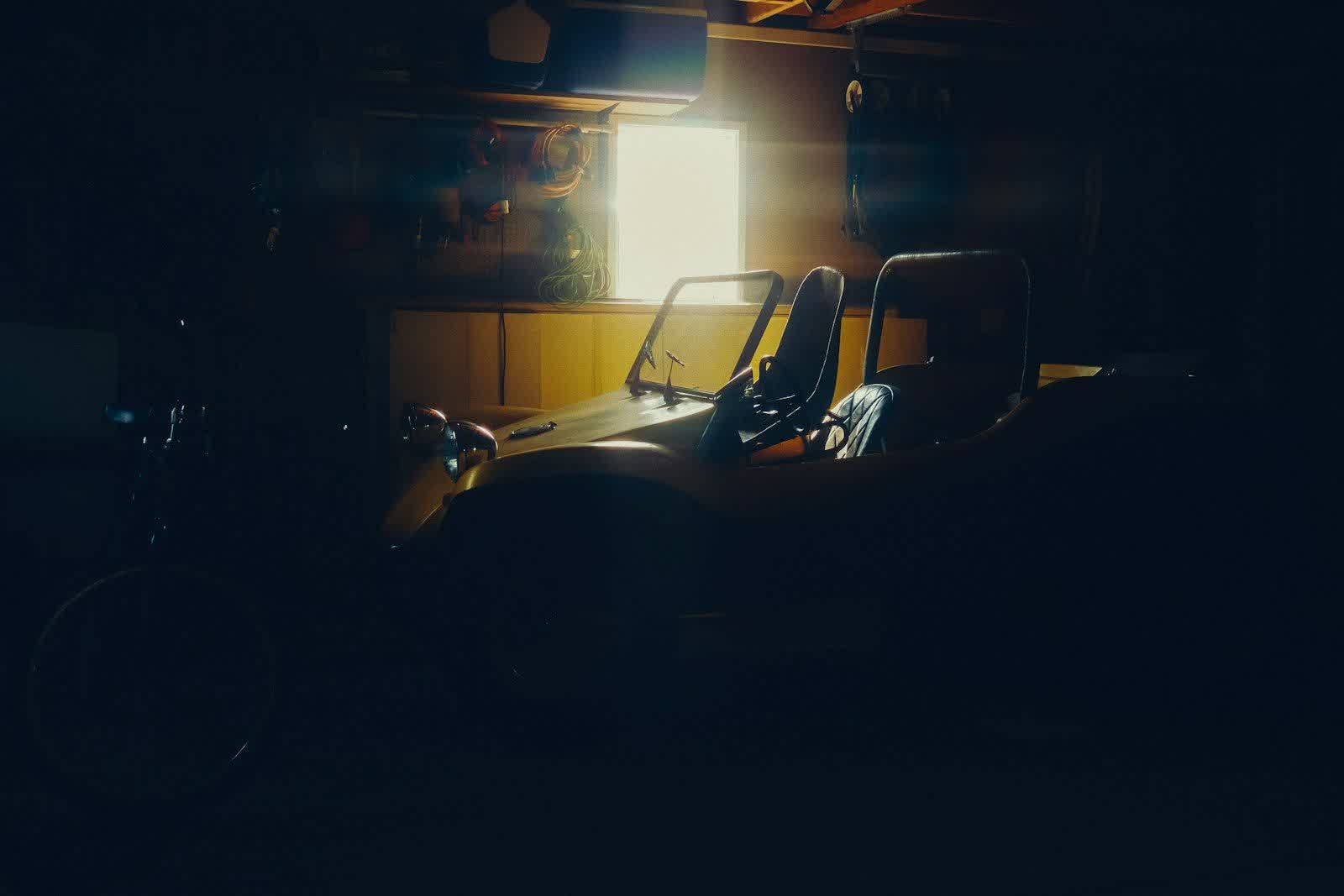 A low open-top car in a dark garage lit by a single window