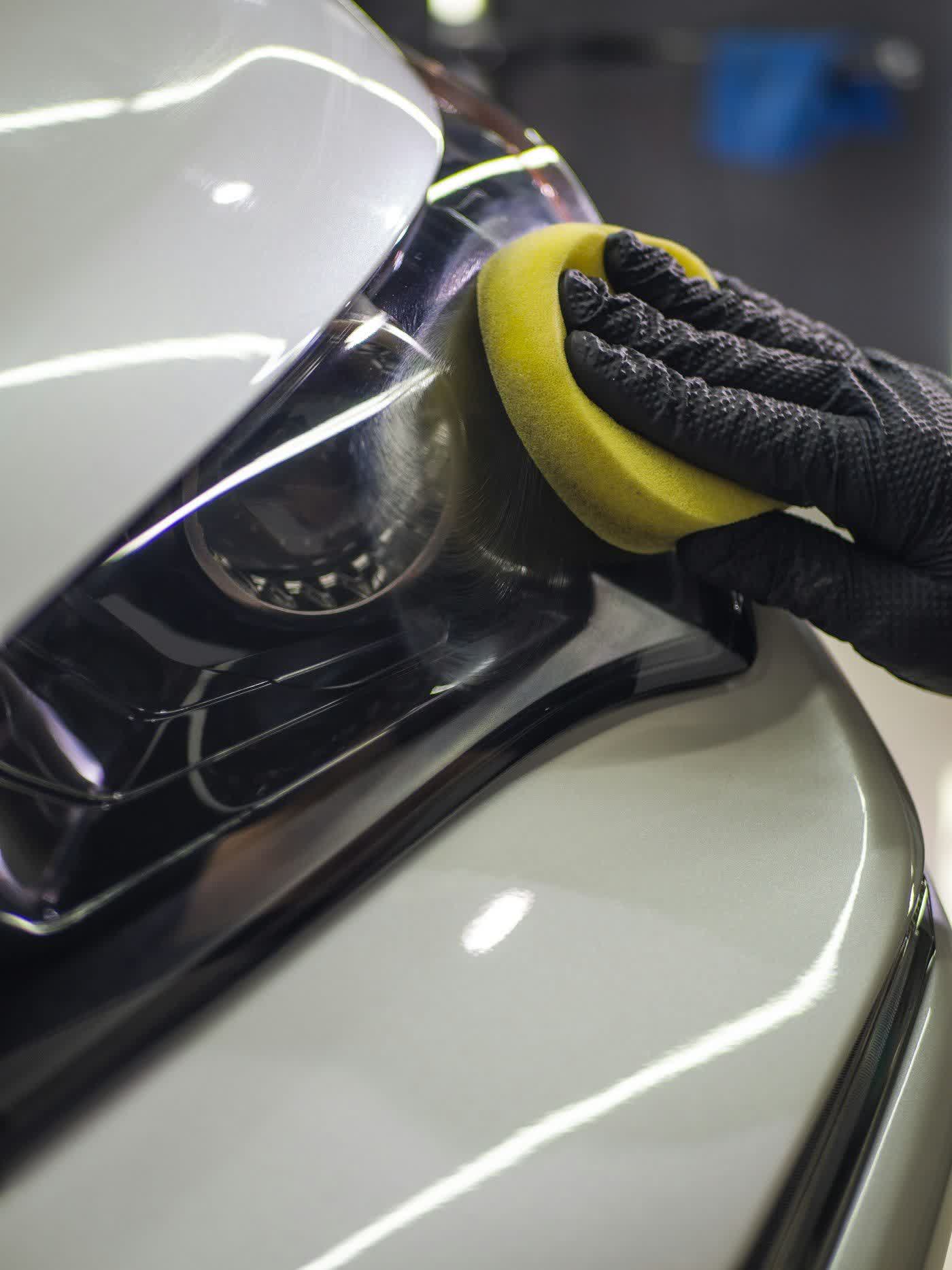 Gloved hand levelling coating across a panel with an applicator pad